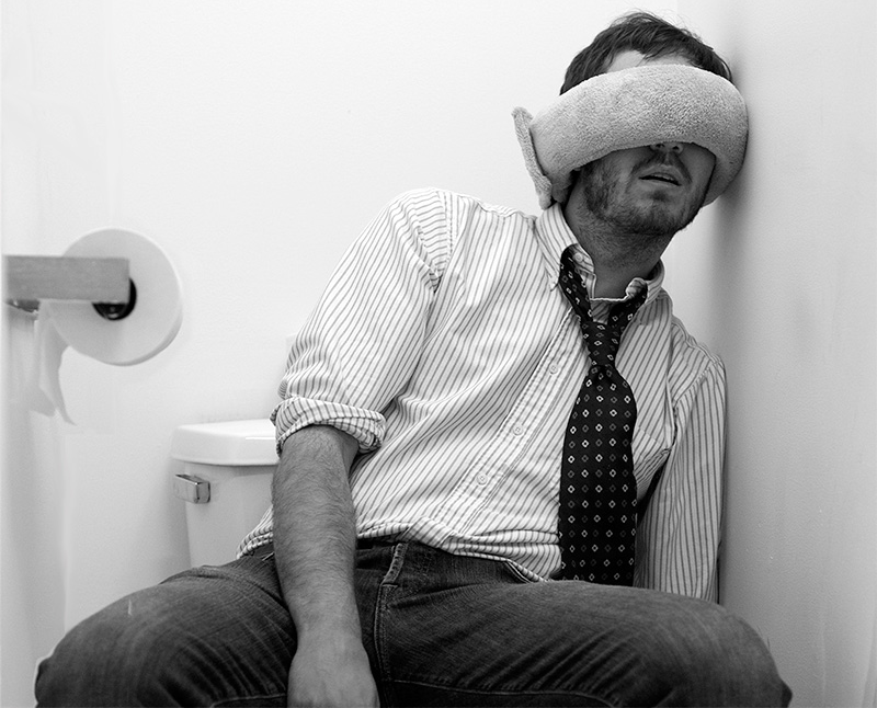 A man napping on the toilet wearing the Wrap-a-Nap
